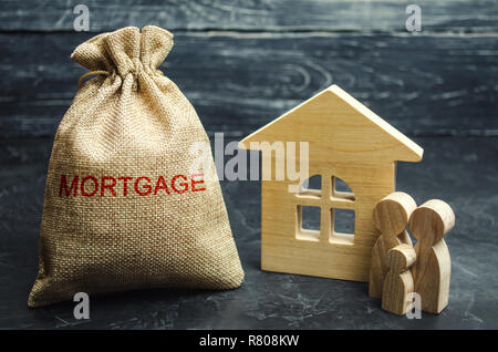 Ein Beutel mit Geld und das Wort Hypothek und ein Holzhaus. Die Anhäufung von Geld Zinsen auf Hypotheken zu bezahlen. Kauf einer Immobilie in der Schuld. Ta Stockfoto