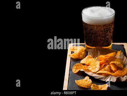 Glas Lagerbier mit Kartoffelchips Snack auf Stein Board auf schwarzem Hintergrund. Stockfoto