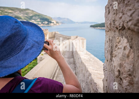 Kaukasische Frau mit einem blauen Hut, die Bilder von den historischen Mauern der Altstadt von Dubrovnik, Kroatien im Sommer Stockfoto