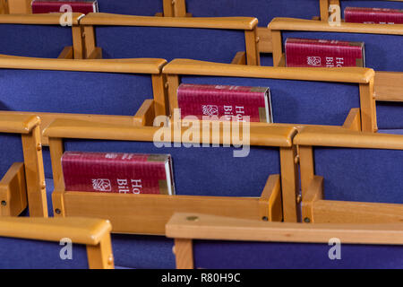 Brockenhurst, England - 23. Oktober 2018: Rote heiligen Bibeln auf einem blauen Stühle in der Kirche von New Milton. Stockfoto