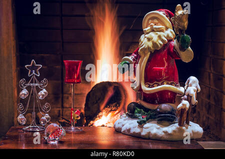 Weihnachtsdekoration mit Santa Claus, Crystal Christmas Tree, rot Likör Glas und Granatapfel. Die Flamme der Kamin im Hintergrund. Stockfoto