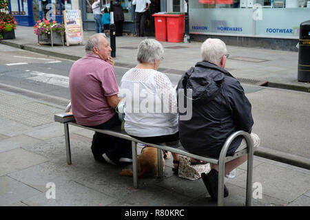 Drei Rentner sitzen auf einer Bank auf einer Höhe Straße in Wells, Somerset. Stockfoto