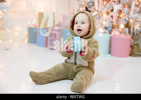 Fröhliches Kind mit einem Geschenk an das Neue Jahr. Ein Jahr alter Junge gekleidet wie ein Reh mit einer Weihnachtsüberraschung Stockfoto