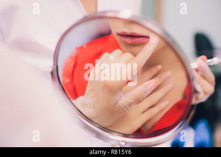 Junge Frau bekommt eine Injektion in die Lippen im Beauty Salon. Schönheit Injektionen - liegende Frau in der kosmetikerin Büro. Lippen durch Hyaluronsäure, Konturierung Verfahren, Revitalisierung Stockfoto