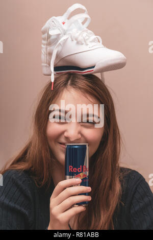 Gerne weibliche Teenager feiern Sie 16 Jahre, dumm mit brandneuer Sneaker auf Kopf und das Trinken aus einer Dose Red Bull Energy Drink. Stockfoto