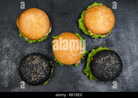 Drei Hamburger mit Rindfleisch Burger und frischem Gemüse auf dunklem Hintergrund. Leckeres Essen. Stockfoto