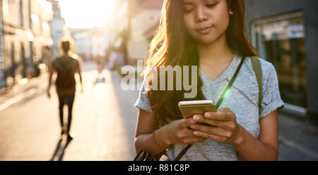 Junge asiatische Frau steht auf einer Straße mit Ihrem Handy Stockfoto