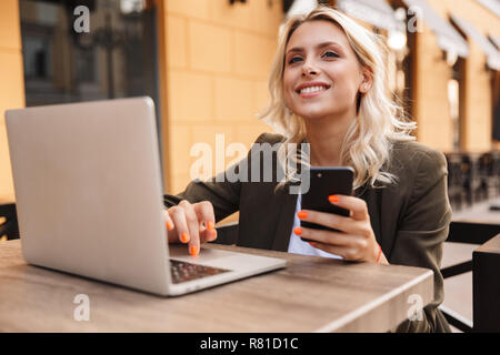 Portrait von Gerne blonde Frau tragen Jacke mit silber Laptop und Smartphone, während im Cafe sitzen im Freien Stockfoto