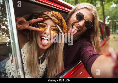 Foto des schönen hipster Paar lächelnd und mit Frieden Zeichen während der Fahrt retro minivan im Wald Stockfoto