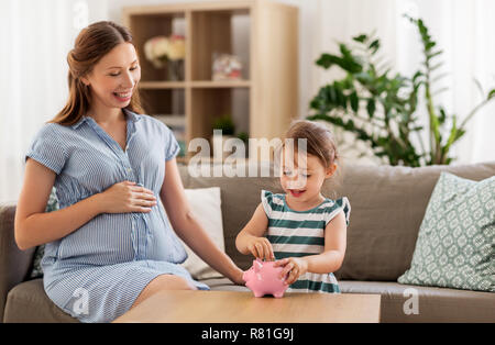 Schwangere Mutter und Tochter mit Sparschwein Stockfoto