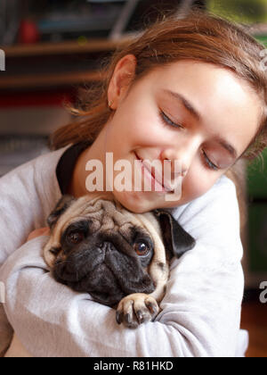 Ziemlich glücklich lächelnden Teenager Mädchen umarmt niedliche Mops Hund mit Liebe Stockfoto