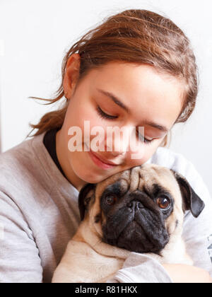 Ziemlich glücklich lächelnden Teenager Mädchen umarmt niedliche Mops Hund mit Liebe Stockfoto