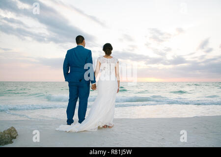 Neu jungen verheirateten männlichen Mann und Frau Frau, Hände auf den Strand mit Blick auf das Meer Horizont bei Sentset nach Hochzeit Stockfoto