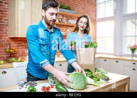 Junges Paar der Vegetarier auspacken zurück Einkaufen mit frischem Grün Produkt auf die Küche zu Hause. Stockfoto