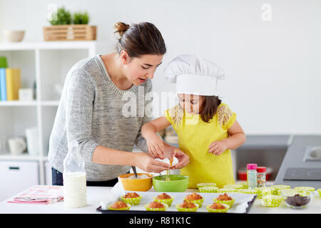 Glückliche Mutter und Tochter backen Muffins zu Hause Stockfoto