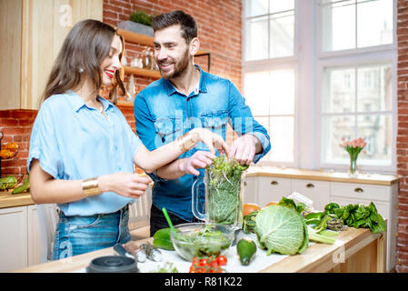 Junge paar Vegetarier in blauen Shirts Smoothie mit frischem Grün Produkte auf die Küche zu Hause. Stockfoto