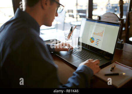 Nahaufnahme Rückansicht der kaukasischen Geschäftsmann Hände schreiben auf Laptop Tastatur und Touchpad. Notebook und Pen in Vordergrund der Arbeitsbereich. Diagramme und Grafiken auf dem Bildschirm. Isolierte kein Gesicht sehen. Stockfoto