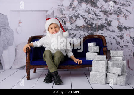 Der junge öffnet Geschenke vom Weihnachtsmann. Studio gedreht. Im Hintergrund ein weißer Weihnachtsbaum. Stockfoto