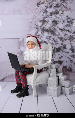 Der junge öffnet Geschenke vom Weihnachtsmann. Studio gedreht. Im Hintergrund ein weißer Weihnachtsbaum. Stockfoto