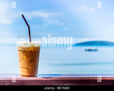Eistee mit Milch oder traditionelle Thai Tee in durchsichtigen Glas mit Stroh auf Holz- bar auf blauen Himmel und seascape Hintergrund auf Sonnenschein Tag mit Co Stockfoto