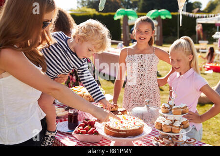 Kinder, die an Kuchen Abschaltdruck am beschäftigten Sommer Garten Fete Stockfoto