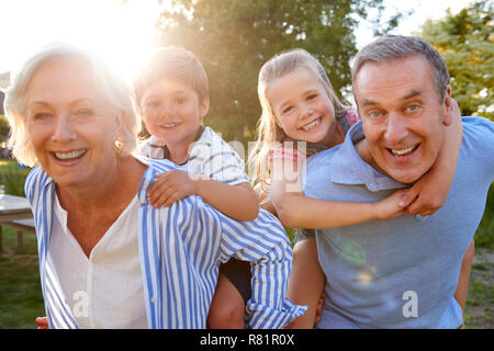Portrait von lächelnden Großeltern und Enkelkinder Piggyback Ride im Freien im Sommer Park Stockfoto