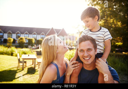 Porträt der Familie mit Vater Sohn Fahrt auf Schultern in der Garten der Sommer Pub Stockfoto