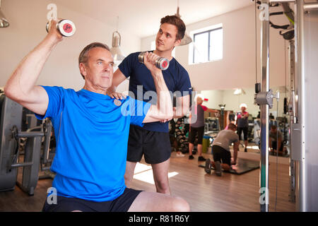 Ältere Menschen Trainieren mit Gewichten wird gefördert vom persönlichen Trainer im Fitnessraum Stockfoto