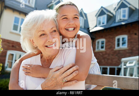 Enkelin umarmen Großmutter auf der Bank während eines Besuchs in den Ruhestand Home Stockfoto