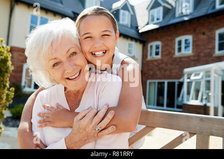 Portrait von Enkelin umarmen Großmutter auf der Bank während eines Besuchs in den Ruhestand Home Stockfoto