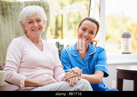 Portrait der älteren Frau sitzt im Stuhl mit Krankenschwester im Ruhestand Home Stockfoto