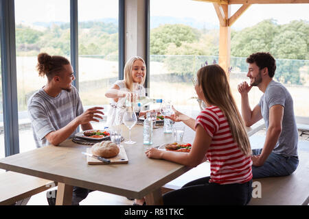 Junge Frau gießen Wein für die Freunde am Tisch sitzen während einer Party zu feiern, in der Nähe Stockfoto
