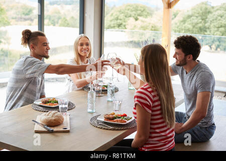 Vier junge erwachsene Freunde feiern bei einem Abendessen ihre Weingläser anheben, in der Nähe Stockfoto