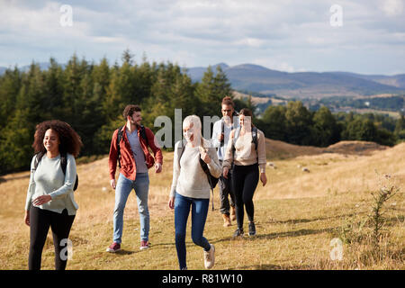 Multi-ethnische Gruppe von fünf glückliche junge erwachsene Freunde sprechen, da Sie auf einem ländlichen weg während einer Wanderung zu Fuß Stockfoto