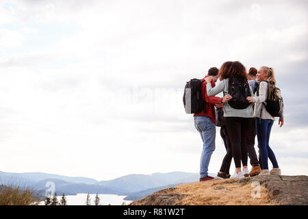 Eine Gruppe von fünf gemischten Rennen junge erwachsene Freunde umarmen nach Ankunft auf dem Gipfel während der Wanderung, in der Nähe Stockfoto