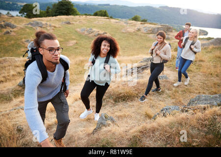 Eine multi-ethnische Gruppe von fünf jungen Erwachsenen Freunde Lächeln beim Klettern auf den Gipfel während einer Bergwanderung, in der Nähe Stockfoto