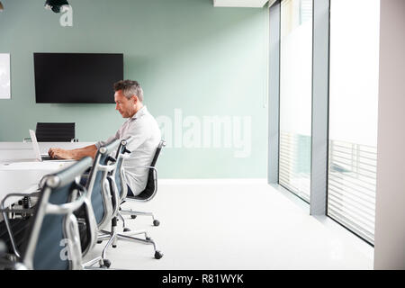 Leger gekleidet Reife Geschäftsmanns, der auf dem Laptop am Konferenztisch im Tagungsraum Stockfoto