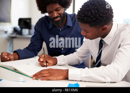 High School Tutor, Uniformierte männliche Kursteilnehmer Einzelunterricht am Schreibtisch im Klassenzimmer Stockfoto