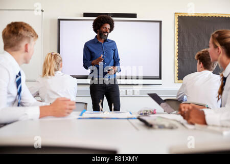 Männliche High School Lehrer Neben interaktiven Whiteboard und Lehre Lehre Schüler Uniform tragen Stockfoto