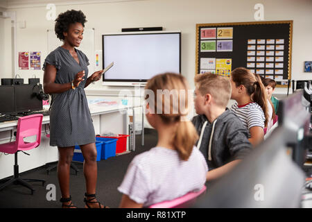 Lehrer mit digitalen Tablet im Gespräch mit der High School Kursteilnehmer sitzen durch Bildschirme im Computer Klasse Stockfoto
