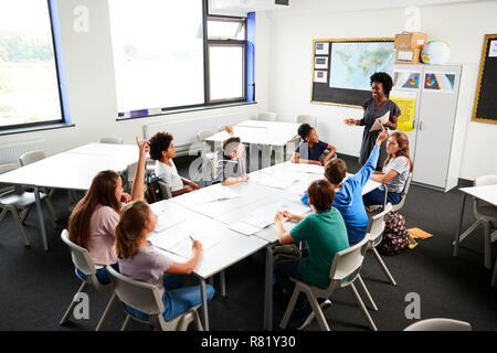 High School Schüler heben die Hände zu beantworten Frage durch den Lehrer im Klassenzimmer Stockfoto