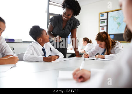 Weibliche High School Lehrer helfen den Studenten das Tragen einheitlicher Sitzen um die Tische herum In Lektion Stockfoto