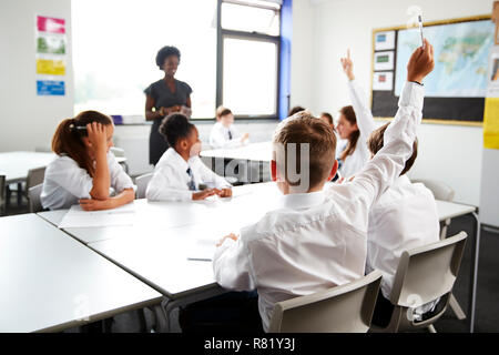 Schülerinnen und Schüler tragen Uniform heben die Hände zu beantworten Frage durch den Lehrer im Klassenzimmer Stockfoto