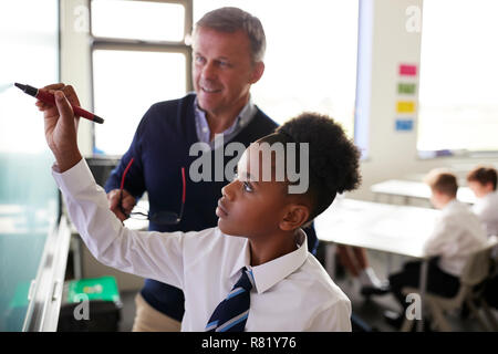 Männliche High School Lehrer mit weiblichen Student trägt die einheitliche Verwendung der interaktiven Whiteboard während der Lektion Stockfoto