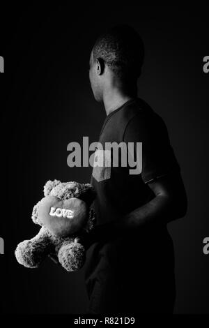 Traurige junge afrikanische Mann mit Teddybär und der Liebe Zeichen Text in Schwarz und Weiß Stockfoto