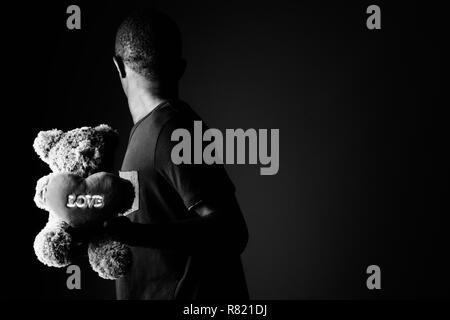 Traurige junge afrikanische Mann mit Teddybär und der Liebe Zeichen Text in Schwarz und Weiß Stockfoto