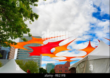 Bunte Schatten Tuch ist gespannt zwischen Bäumen entlang Tom McCall Waterfront Park in Portland, Oregon. Bewölktem Himmel und ein Teil der Skyline der Stadt werden kann Stockfoto