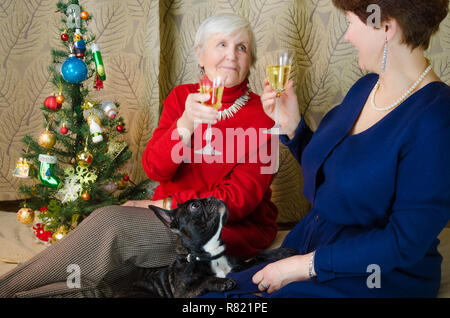 Familie Momente zur Weihnachtszeit. alte Frau lächeln. Großmutter und ihrer Tochter sitzen in der Nähe von Weihnachten Baum. Geist des Neuen Jahres. Clink Gläser mit Champagner. Stockfoto