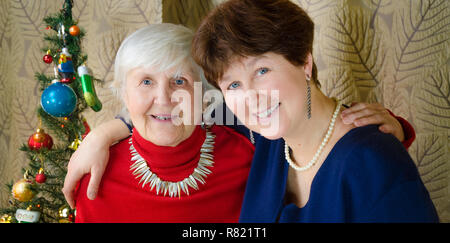 Familie Momente zur Weihnachtszeit. alte Frau lächeln. Großmutter und ihrer Tochter sitzen in der Nähe von Weihnachten Baum. Geist der Neuen Jahr. umarmen sich Stockfoto