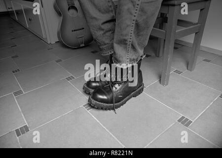 Rock und Roll Konzept. Schwarze Stiefel und klassische Gitarre. Schwarz/Weiß-Bild Stockfoto